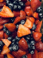 A vibrant close-up photo of fresh mixed fruits including berries, oranges, and apples with honey drizzled over them.