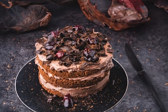 A beautifully decorated black forest cake with fresh cherries and chocolate shavings on a rustic wooden table.