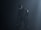 A humanoid robot with dark metallic body stands in a dimly lit environment, emitting an eerie presence. Its eyes glow white, providing a stark contrast to the dark surroundings. The robot's body is detailed with mechanical joints and a circular emblem on its shoulder.