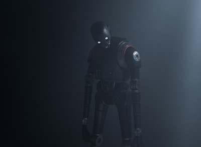 A humanoid robot with dark metallic body stands in a dimly lit environment, emitting an eerie presence. Its eyes glow white, providing a stark contrast to the dark surroundings. The robot's body is detailed with mechanical joints and a circular emblem on its shoulder.