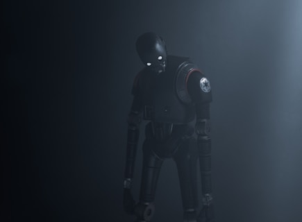 A humanoid robot with dark metallic body stands in a dimly lit environment, emitting an eerie presence. Its eyes glow white, providing a stark contrast to the dark surroundings. The robot's body is detailed with mechanical joints and a circular emblem on its shoulder.