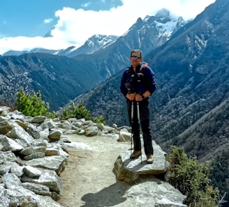 A hiker adjusting trekking poles on a rocky mountain trail under a clear blue sky.