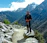 A smiling hiker standing on a rocky Kilimanjaro trail with snow-capped peaks behind.