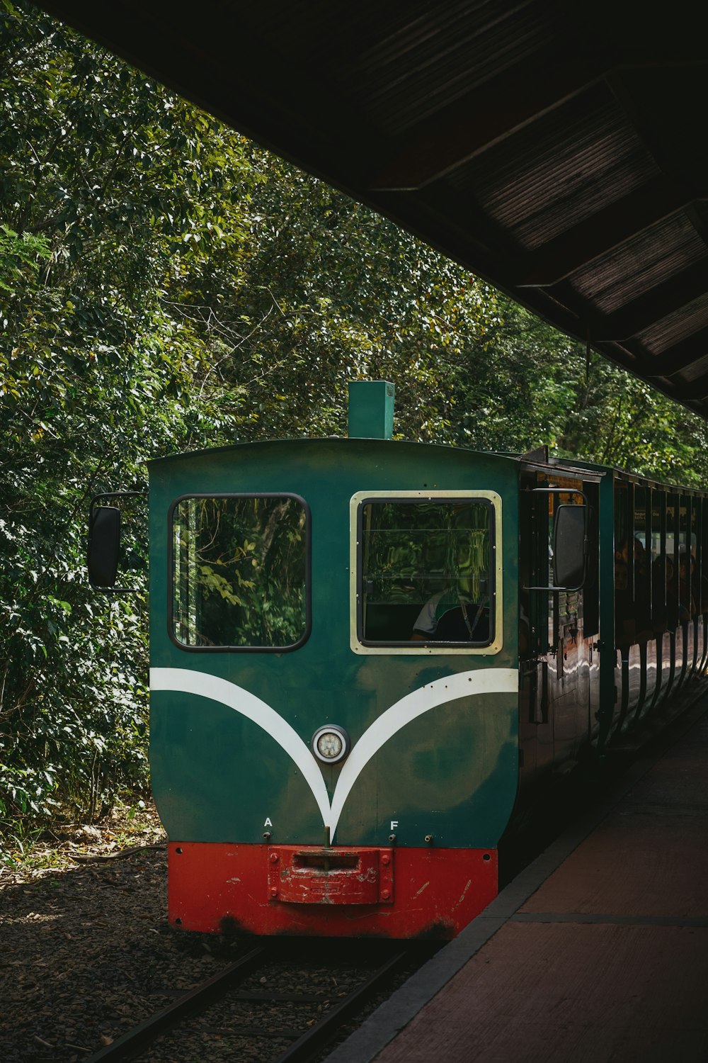 a green train traveling down train tracks next to a forest