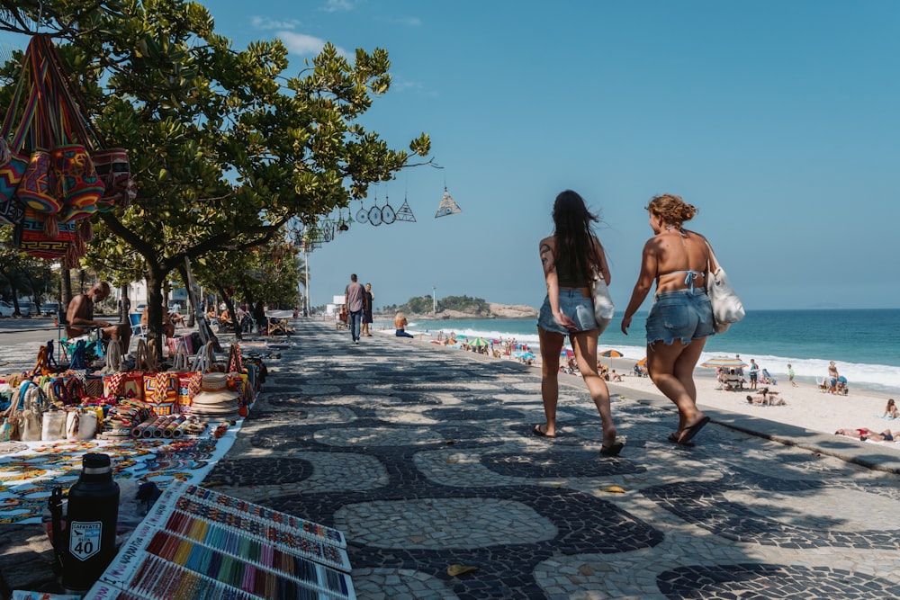 a couple of women walking down a street next to the ocean