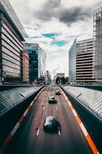 A convoy of transport trucks moving along a city road with modern buildings in the background.