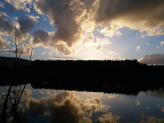 A dramatic sunset over a calm lake with silhouetted trees.