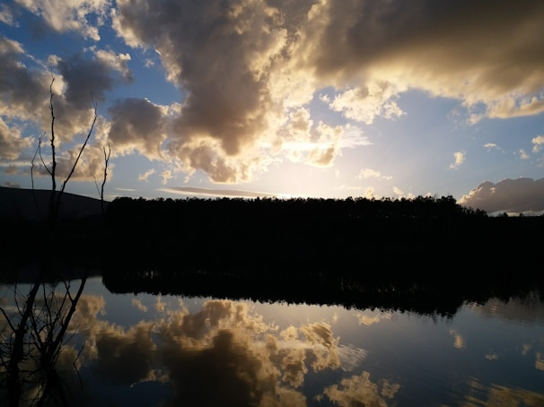 A dramatic sunset over a calm lake with silhouetted trees.