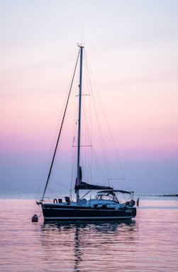 A serene sailboat anchored near a quiet cove at sunset, reflecting calm waters.