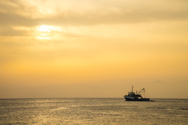 A sleek fishing boat cutting through deep navy waters under a golden sunset sky.