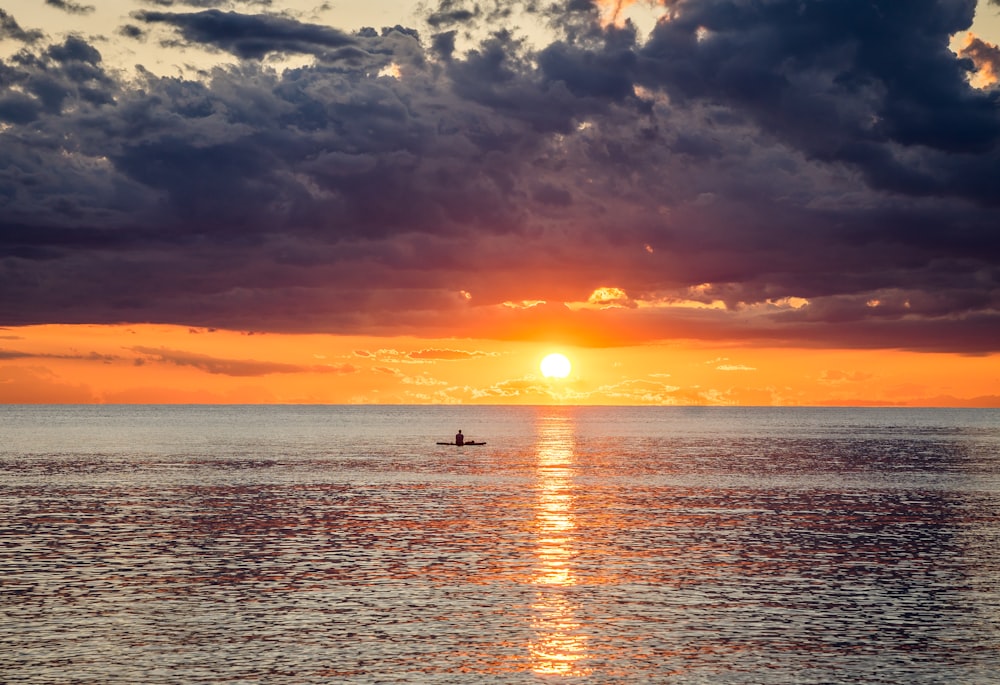 a boat in the ocean at sunset with a cloudy sky