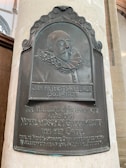 A decorative plaque mounted on a wall depicts a relief portrait of an older man with a ruffled collar. The plaque includes inscriptions in Dutch, commemorating Jan Pieterszoon Sweelinck, a historical figure from 1562-1621.
