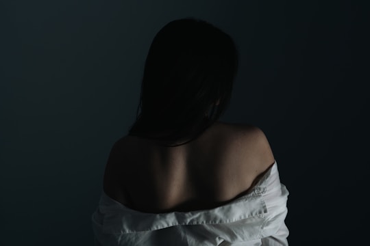A silk robe strap slipping off a shoulder as a figure turns away in a dimly lit room.