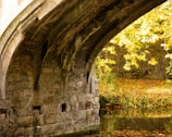 An ancient stone bridge arching over a quiet river surrounded by autumn foliage.