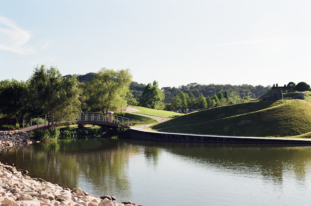 a bridge over a river next to a lush green hillside