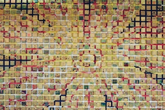 A mosaic composed of numerous small square tiles, each featuring various intricate and colorful drawings. The tiles are predominantly in shades of yellow, creating a sunburst pattern with additional colors like red, green, and black integrated into the design.