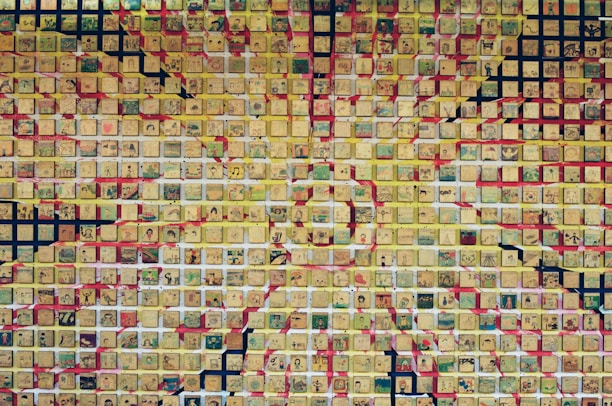 A mosaic composed of numerous small square tiles, each featuring various intricate and colorful drawings. The tiles are predominantly in shades of yellow, creating a sunburst pattern with additional colors like red, green, and black integrated into the design.
