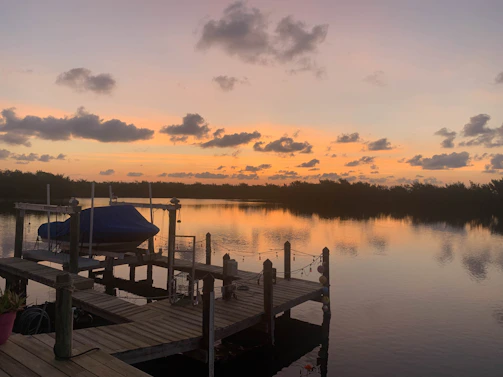 A serene lakeside dock at sunset with a small boat tied gently to the pier.