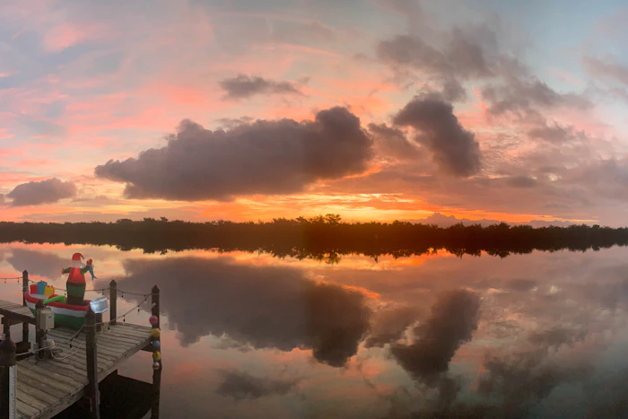 A person sitting on a dock watching the sun over the water