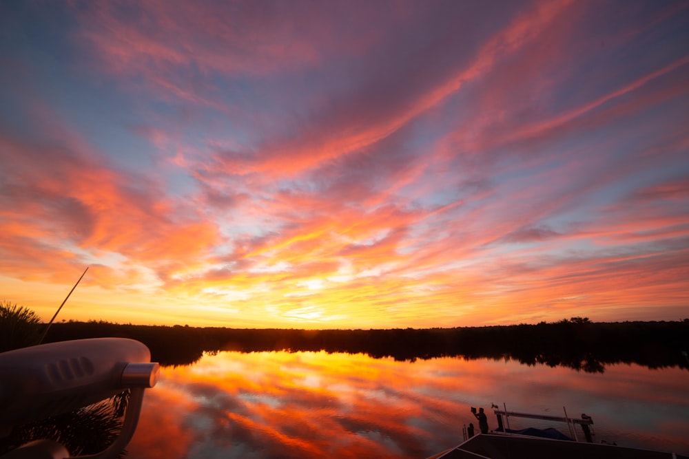 a boat sitting on top of a lake under a colorful sky