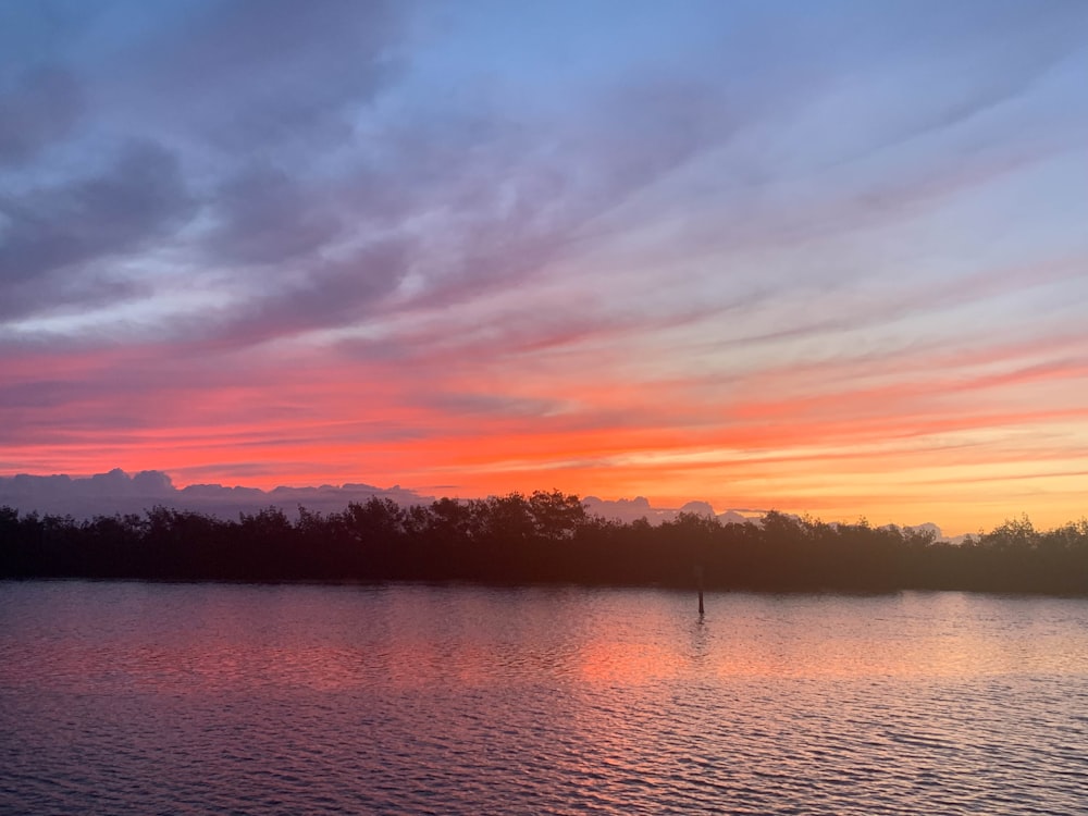 a sunset over a body of water with trees in the background