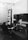 A man is seated at a desk filled with various radio equipment and controls in a room that appears to be an old-fashioned radio or communication station. The equipment includes dials, gauges, and switches along the walls, with a focus on the central console he is operating.
