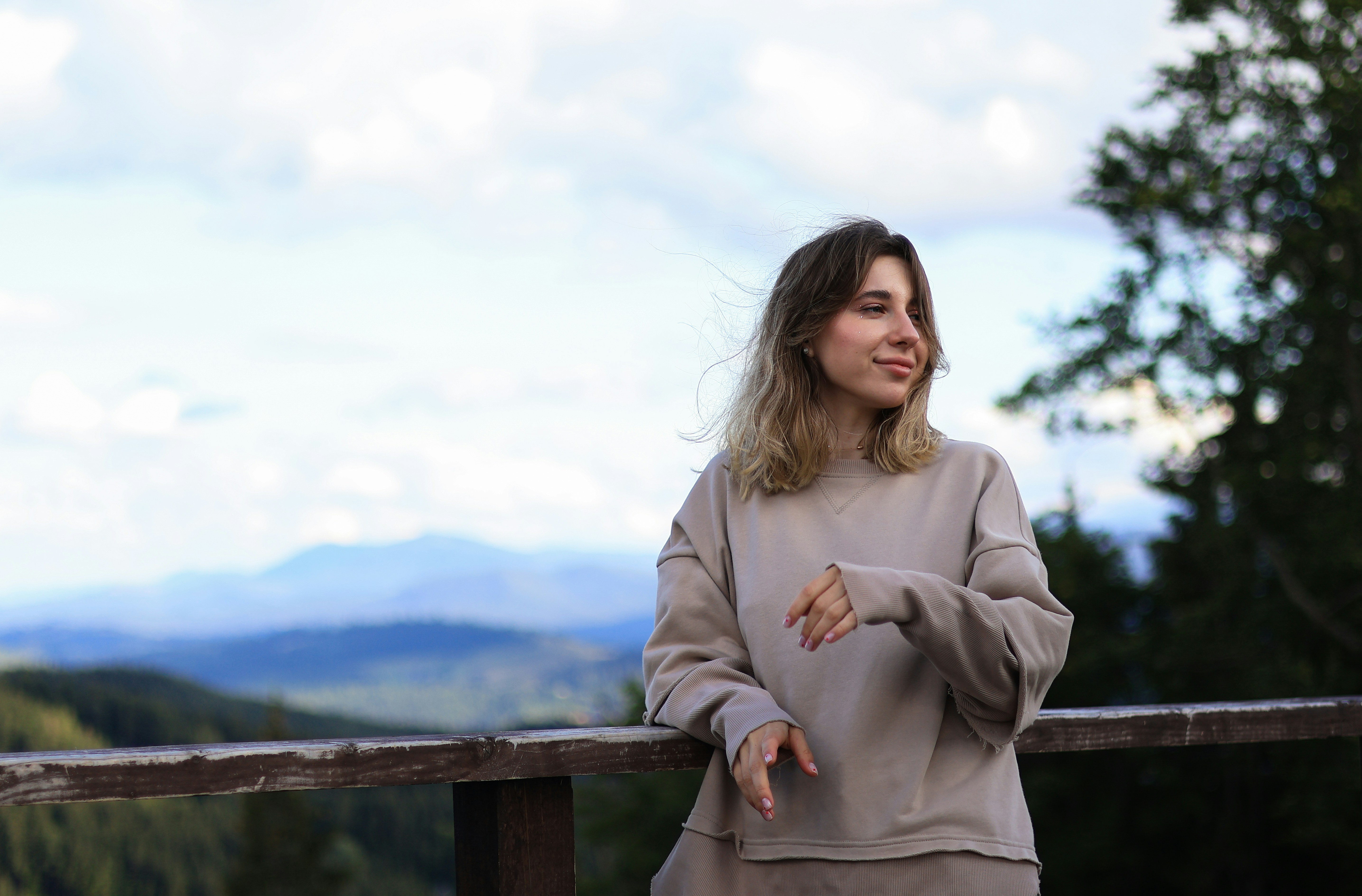 a woman leaning on a rail with mountains in the background