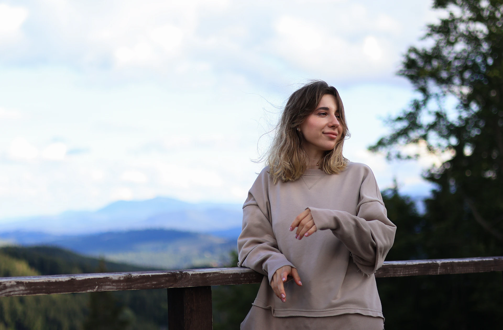 a woman leaning on a rail with mountains in the background
