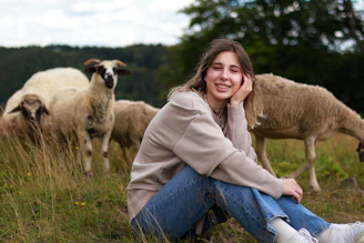 a woman sitting in a field with sheep