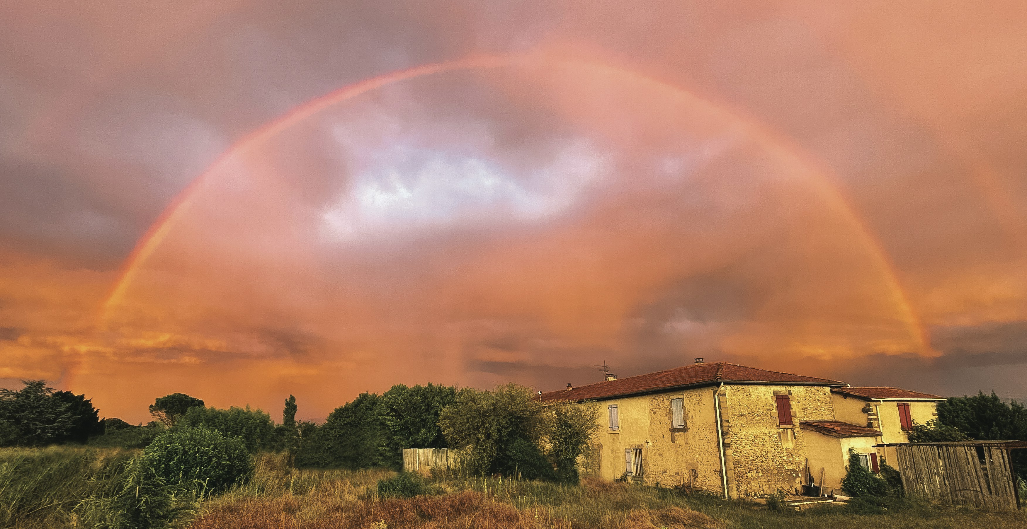 Un double arc-en-ciel apparaît au-dessus d’une maison dans un champ