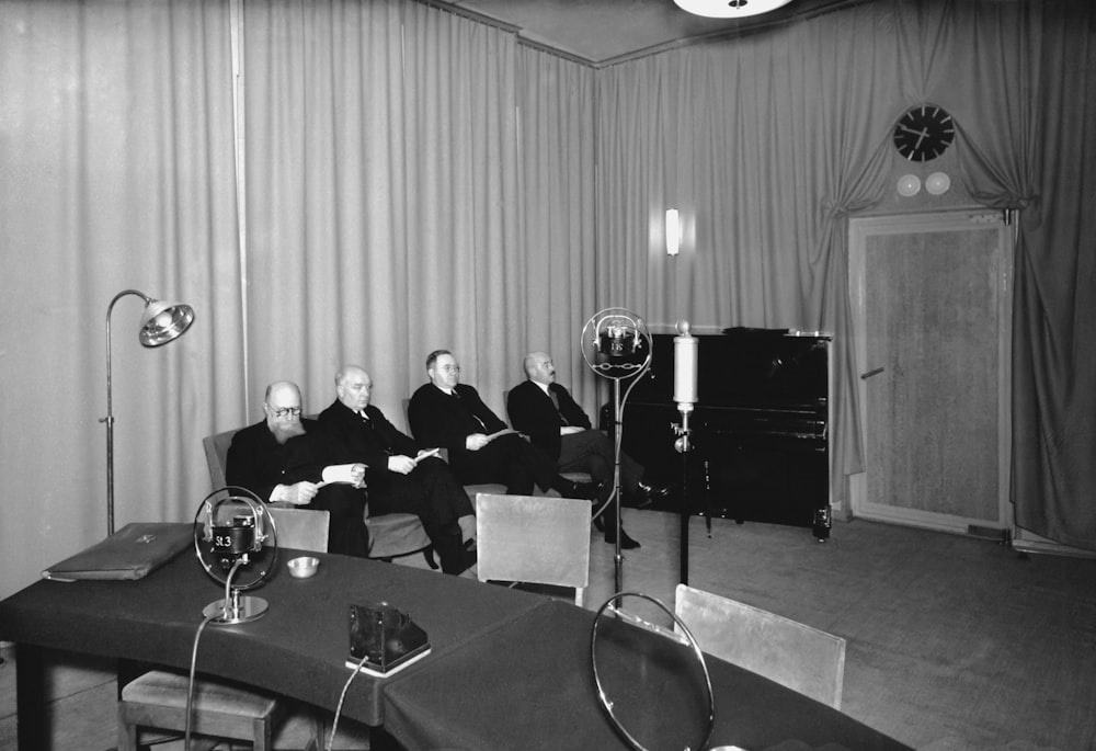 a black and white photo of a group of men sitting in a room