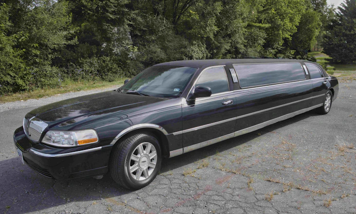 A sleek black limousine parked curbside at LaGuardia Airport under soft evening light.