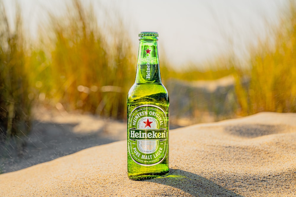 a bottle of beer sitting on top of a sandy beach