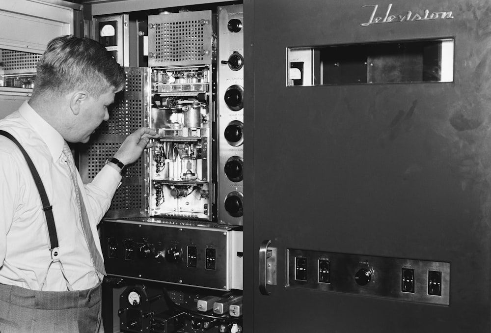 a man in suspenders looking at a machine