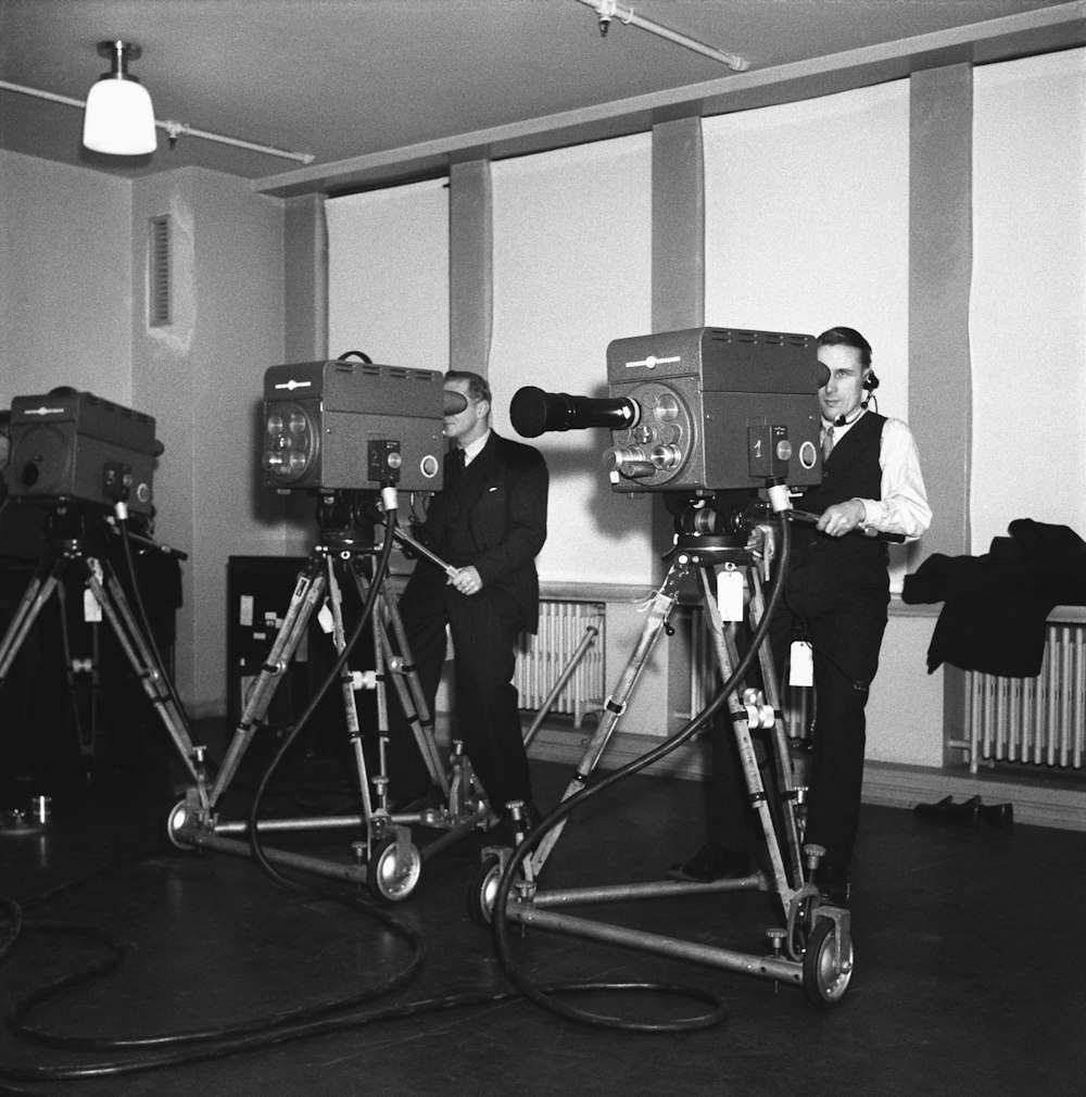 a couple of men standing next to each other in front of a camera