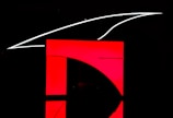 A dark background highlights a bold red and black geometric design. A prominent red rectangular shape dominates the image with a curve intersecting it, creating a modern, minimalist look. Above the red area, a sleek white line extends in a curved manner.