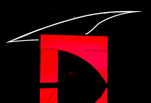 A dark background highlights a bold red and black geometric design. A prominent red rectangular shape dominates the image with a curve intersecting it, creating a modern, minimalist look. Above the red area, a sleek white line extends in a curved manner.