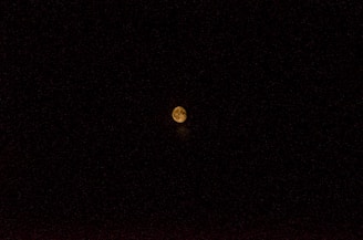 A celestial body, likely the moon, is centered in a vast expanse of black sky. It glows with a warm, yellowish hue, and some surface details such as craters are faintly visible.