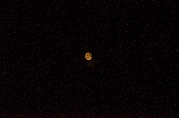 A celestial body, likely the moon, is centered in a vast expanse of black sky. It glows with a warm, yellowish hue, and some surface details such as craters are faintly visible.