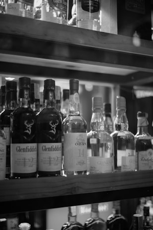 A collection of various whiskey bottles is arranged on wooden shelves. The labels on the bottles are clearly visible, showcasing different brands and types of whiskey.