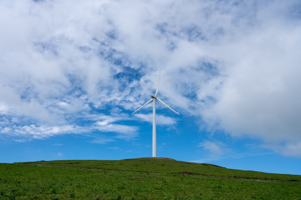 a wind turbine on a grassy hill under a cloudy blue sky