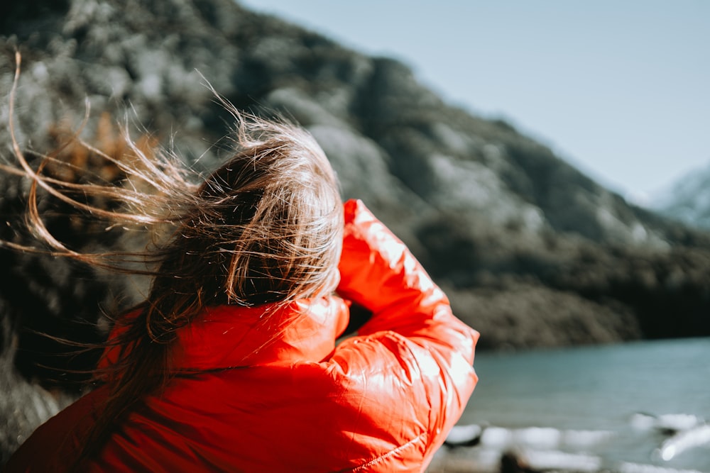 a woman in a red jacket looking at the water