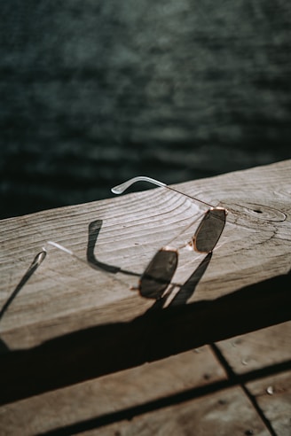Close-up of stylish sunglasses resting on a wooden table with sunlight casting warm shadows