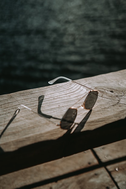 Close-up of stylish sunglasses resting on a wooden table with sunlight casting warm shadows