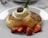A plate with fluffy pancakes topped with a dollop of cream, a small amount of chocolate or caramel topping, and garnished with fresh strawberries and a mint leaf. The setting is light and airy, suggesting a relaxed breakfast or brunch scene.