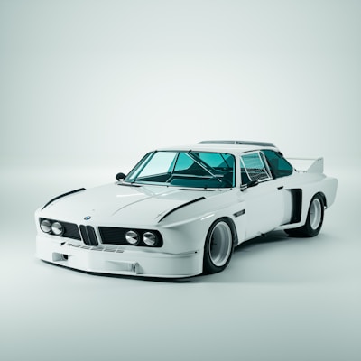 A classic white sports car with sleek aerodynamic features, prominent headlights, and a distinctive grille. The car is parked in a well-lit studio setting with a clean, minimal background. The design includes prominent wheel arches and a rear spoiler.
