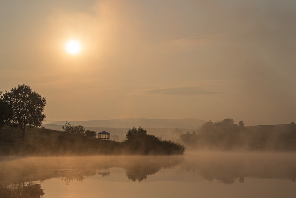 the sun is setting over a lake with fog