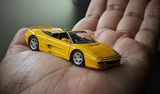 Close-up of a detailed 3D diecast car frame with a hand holding a phone nearby.