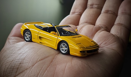 Close-up of a detailed 3D diecast car frame with a hand holding a phone nearby.