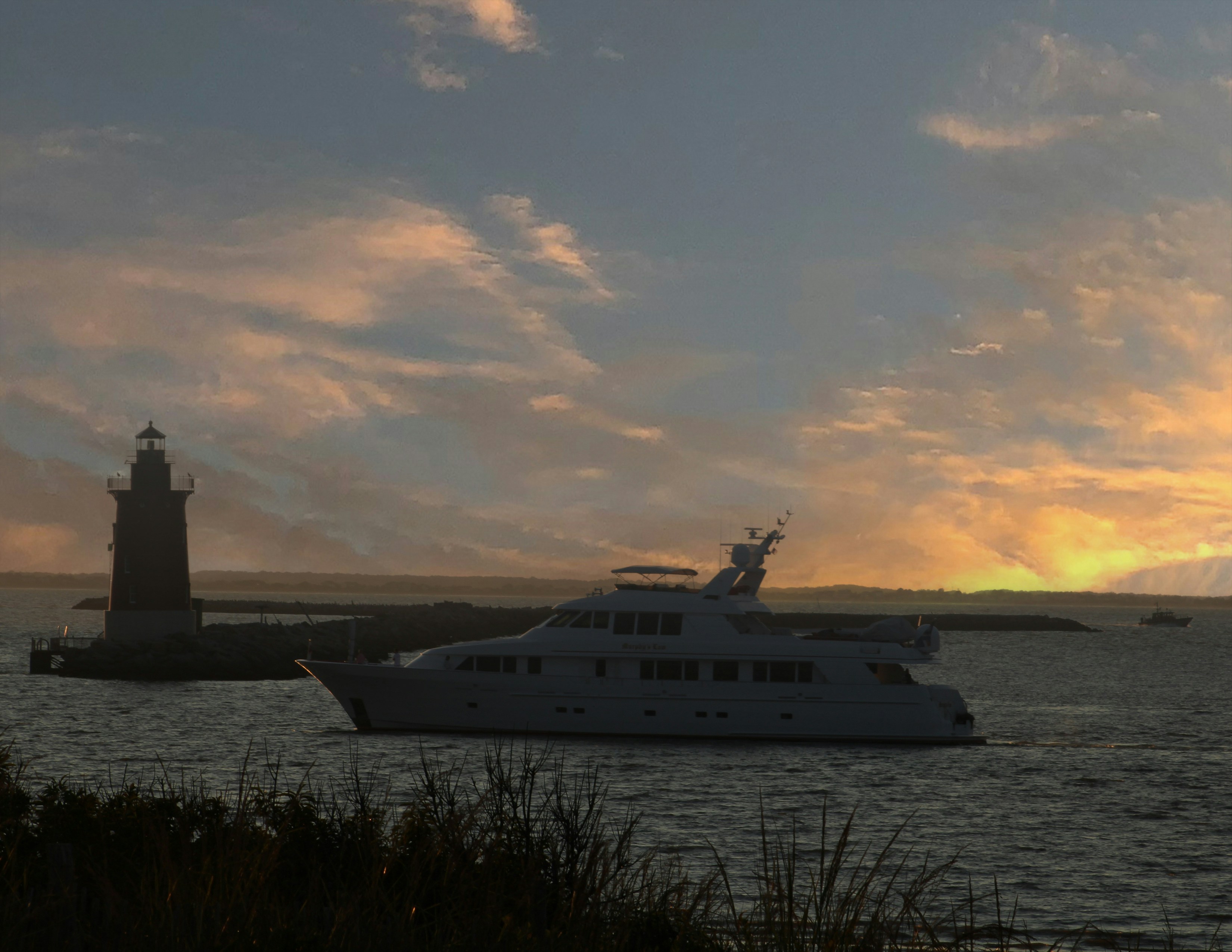 Boat and lighthouse in a bay just off the ocean at sunset.